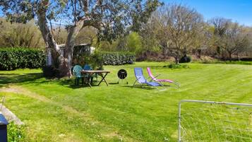 A grassy outdoor area with a table and chairs, a barbecue grill, and a goalpost.