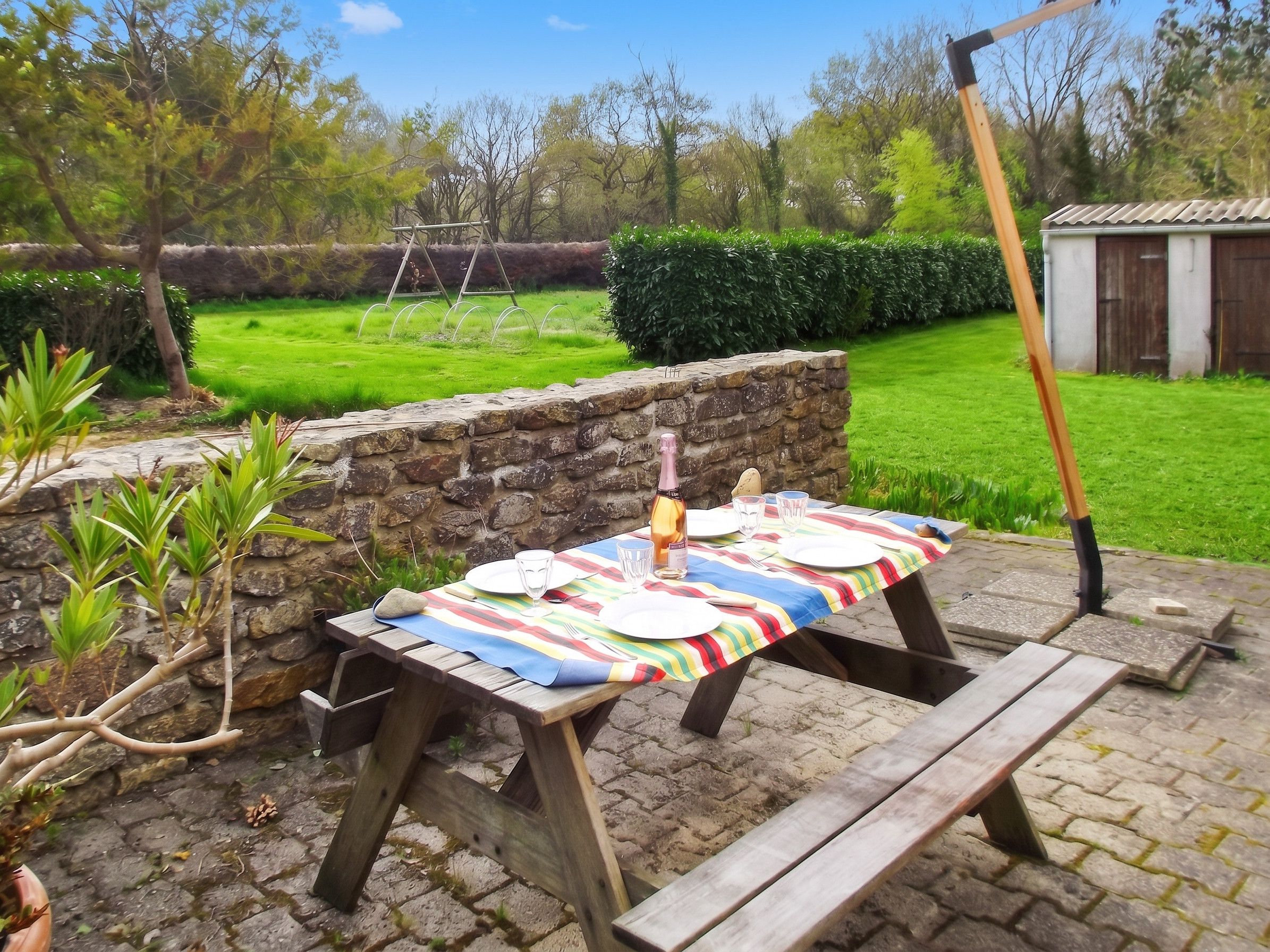 Un área de comedor al aire libre con una mesa de picnic dispuesta para dos personas, rodeada por un muro de piedra y follaje.