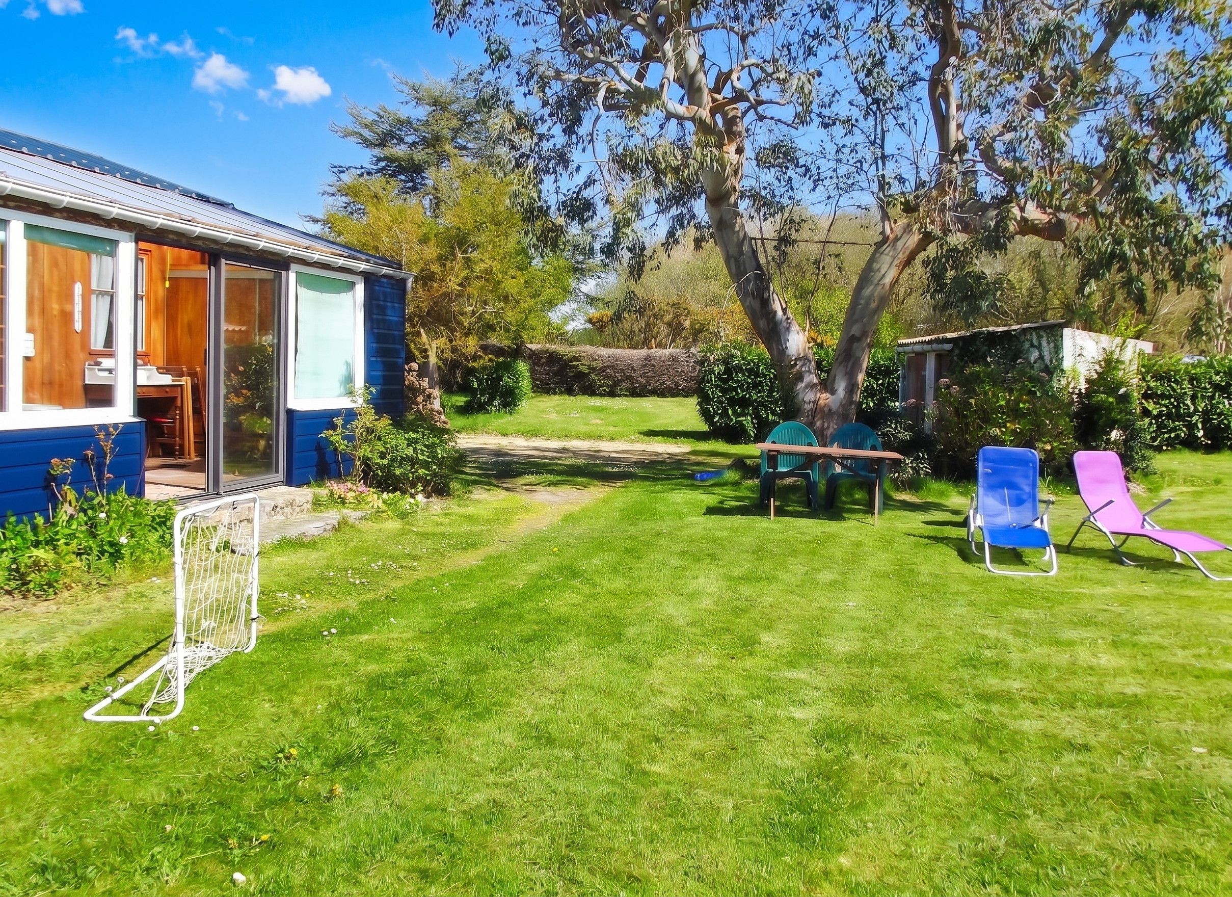 A residential property with a blue house, a lawn, a tree, and outdoor furniture.