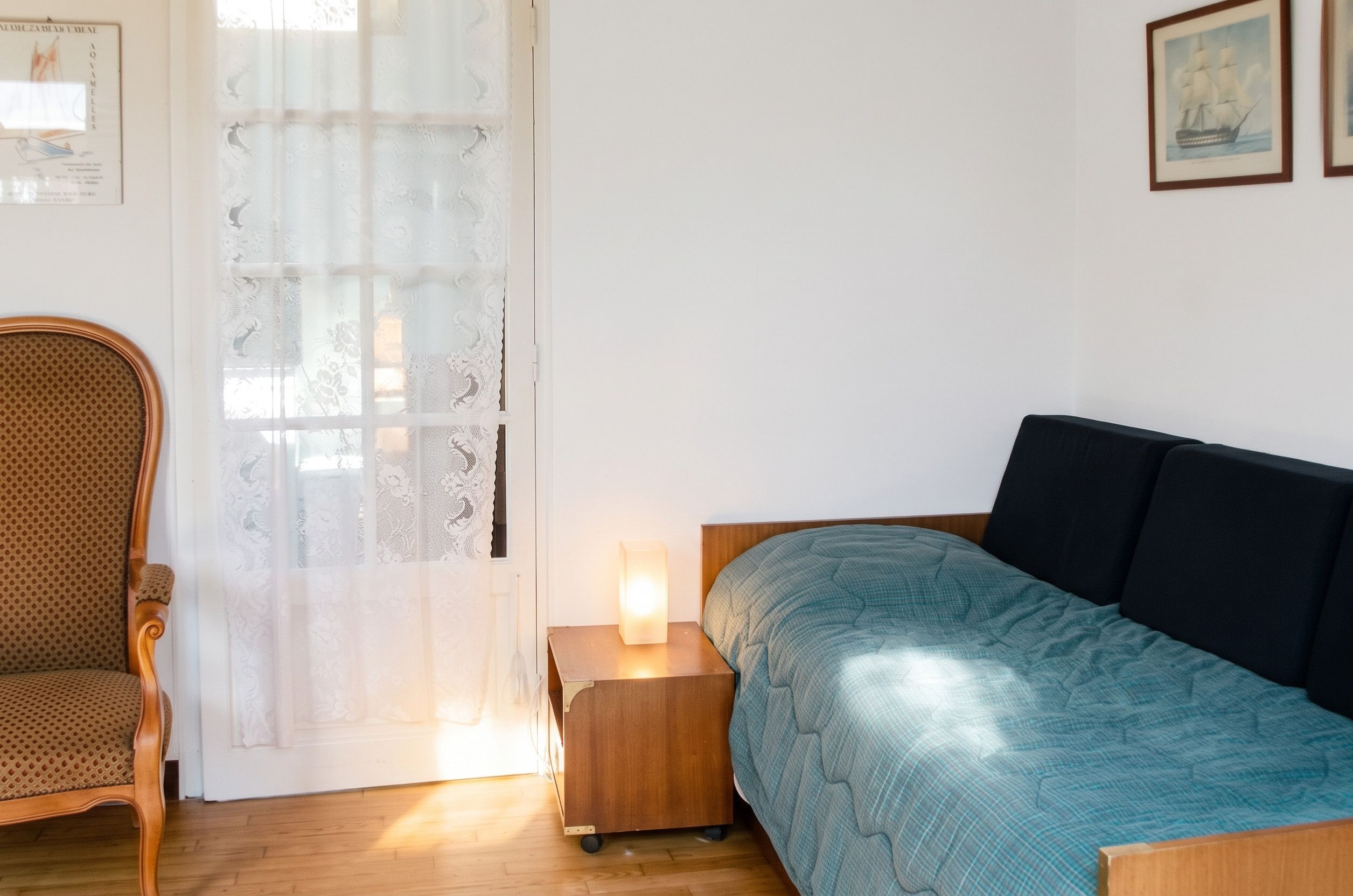 A bedroom with a bed, a chair, a nightstand with a lamp, and a door with a curtain.