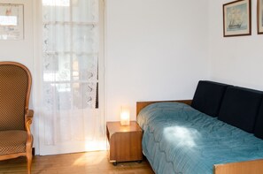 A bedroom with a bed, a chair, a nightstand with a lamp, and a door with a curtain. - Homerez - Charming House in Trédrez-Locquémeau + Garden (Trédrez-Locquémeau)