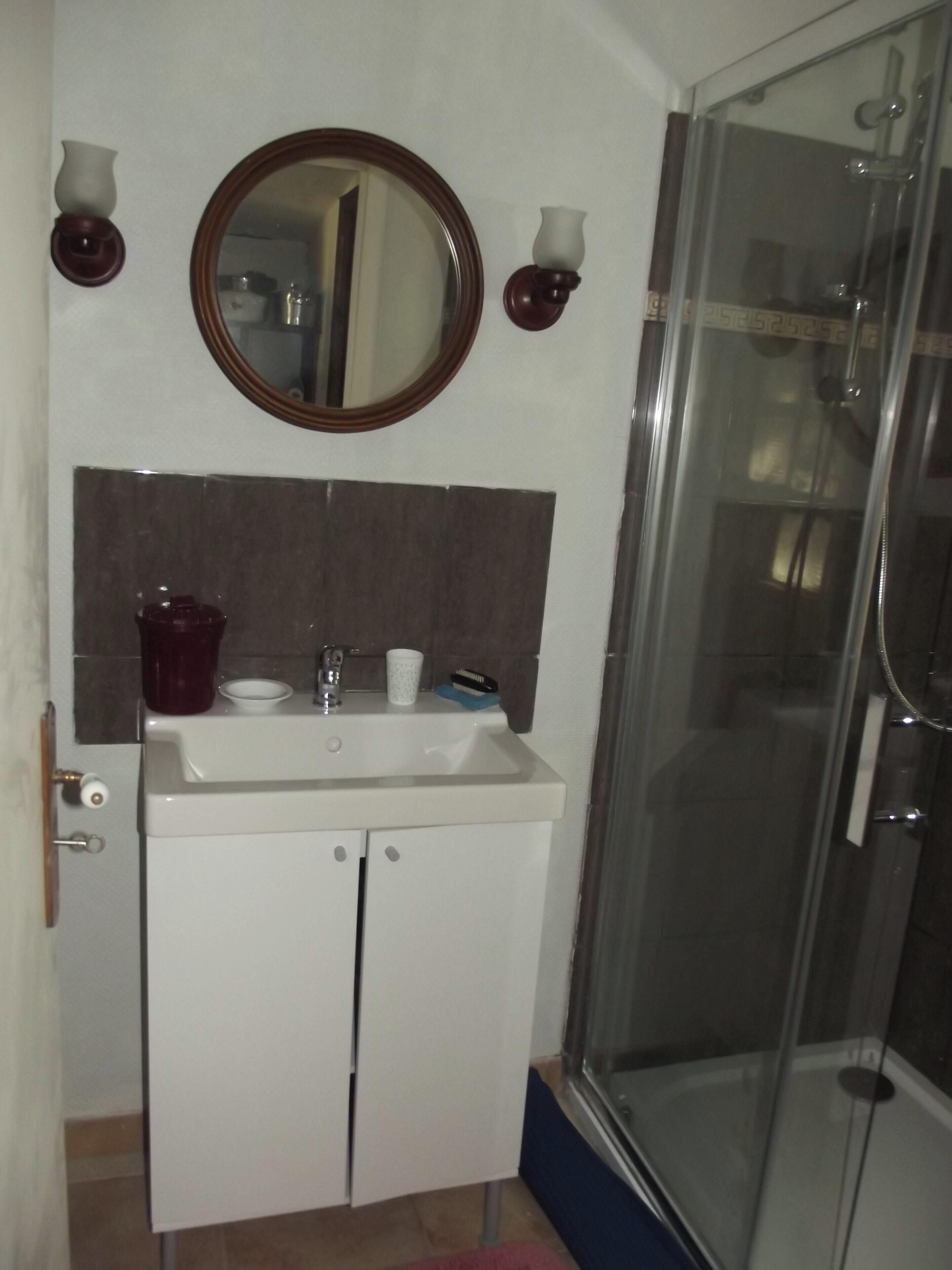 Un baño con lavamanos blanco, espejo y cabina de ducha de vidrio.