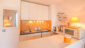 Une cuisine compacte avec des meubles blancs, un plan de travail noir, un four à micro-ondes, un grille-pain et un évier.