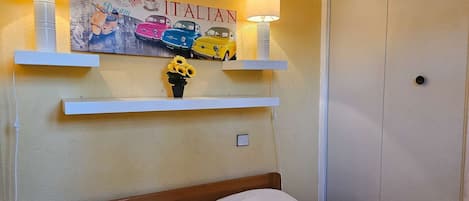 Ein Schlafzimmer mit einem Bett, einem an der Wand befestigten Regal mit Lampe und einer Wanddekoration mit Oldtimern.