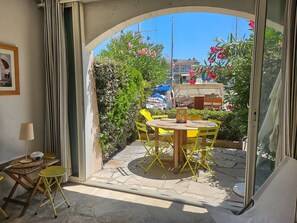 A patio with a table and chairs, a small table with a lamp, and a view of boats and buildings through an archway.