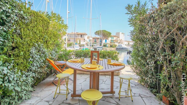 Un espace de restauration en plein air avec une table ronde en bois et des chaises jaunes, le tout entouré de verdure.