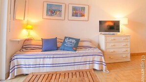 Une chambre à coucher avec un lit, des oreillers, une table de chevet avec une lampe, un téléviseur posé sur une commode et deux tableaux encadrés accrochés au mur.