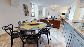 A dining area with a round table, chairs, and a kitchen in the background.