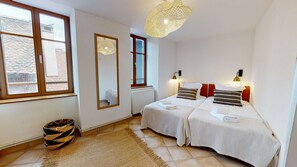 A hotel room with two beds, a large window, a radiator, a woven rug, and a hanging light fixture.