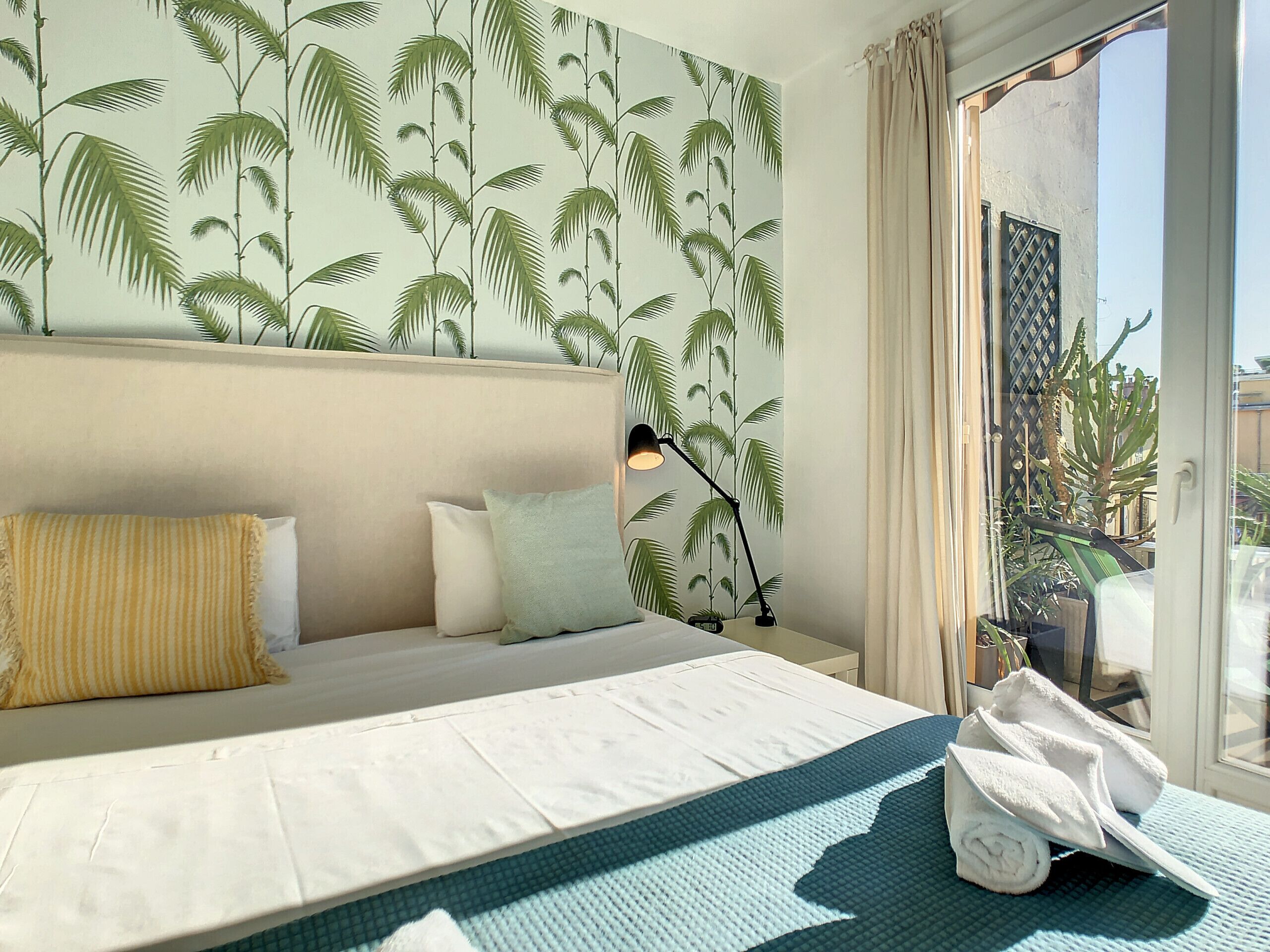 A hotel room with a bed, pillows, a lamp, and a view of the outside.