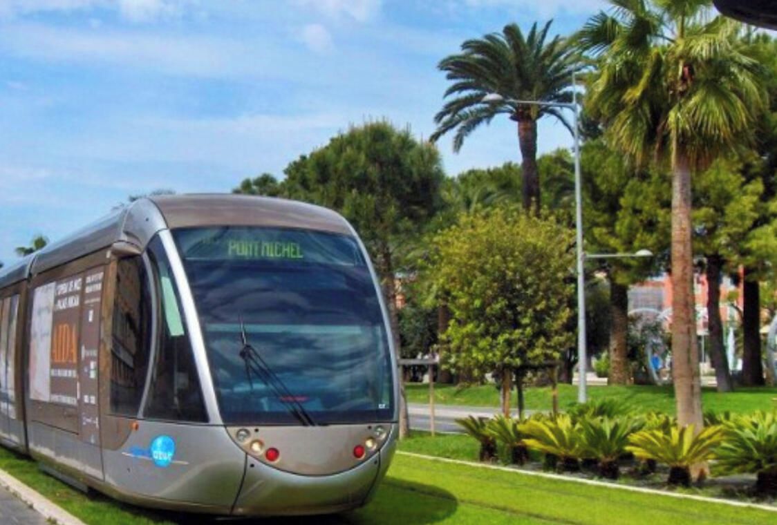 A modern, single-decker bus with 'PONT MICHEL' written on the front, parked in a well-maintained urban area with greenery and palm trees.