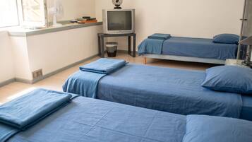Ein Zimmer mit drei Betten, einem Fernseher, einem Ventilator und einer Mülltonne.
