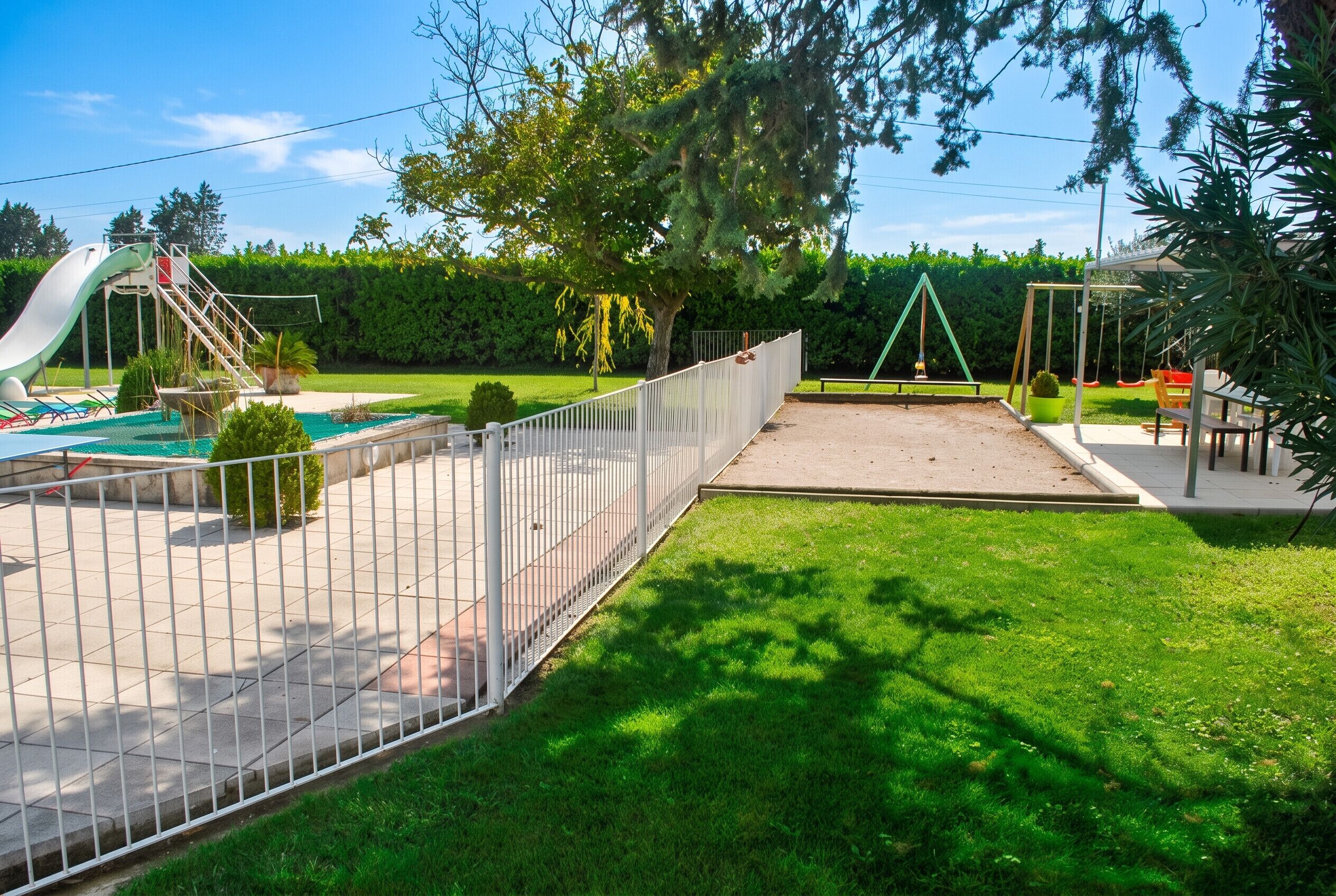 A fenced outdoor area with a slide, a swing set, and a small pool.