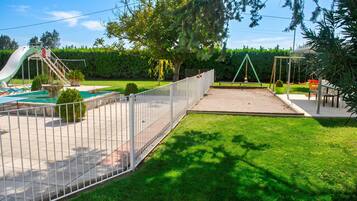 A fenced outdoor area with a slide, a swing set, and a small pool.