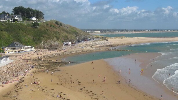 A beach with people sunbathing and swimming, a rocky shoreline, and houses on a hill. - Ground floor apartment with terraces, WIFI, parking, and pets allowed (Barneville-Carteret)