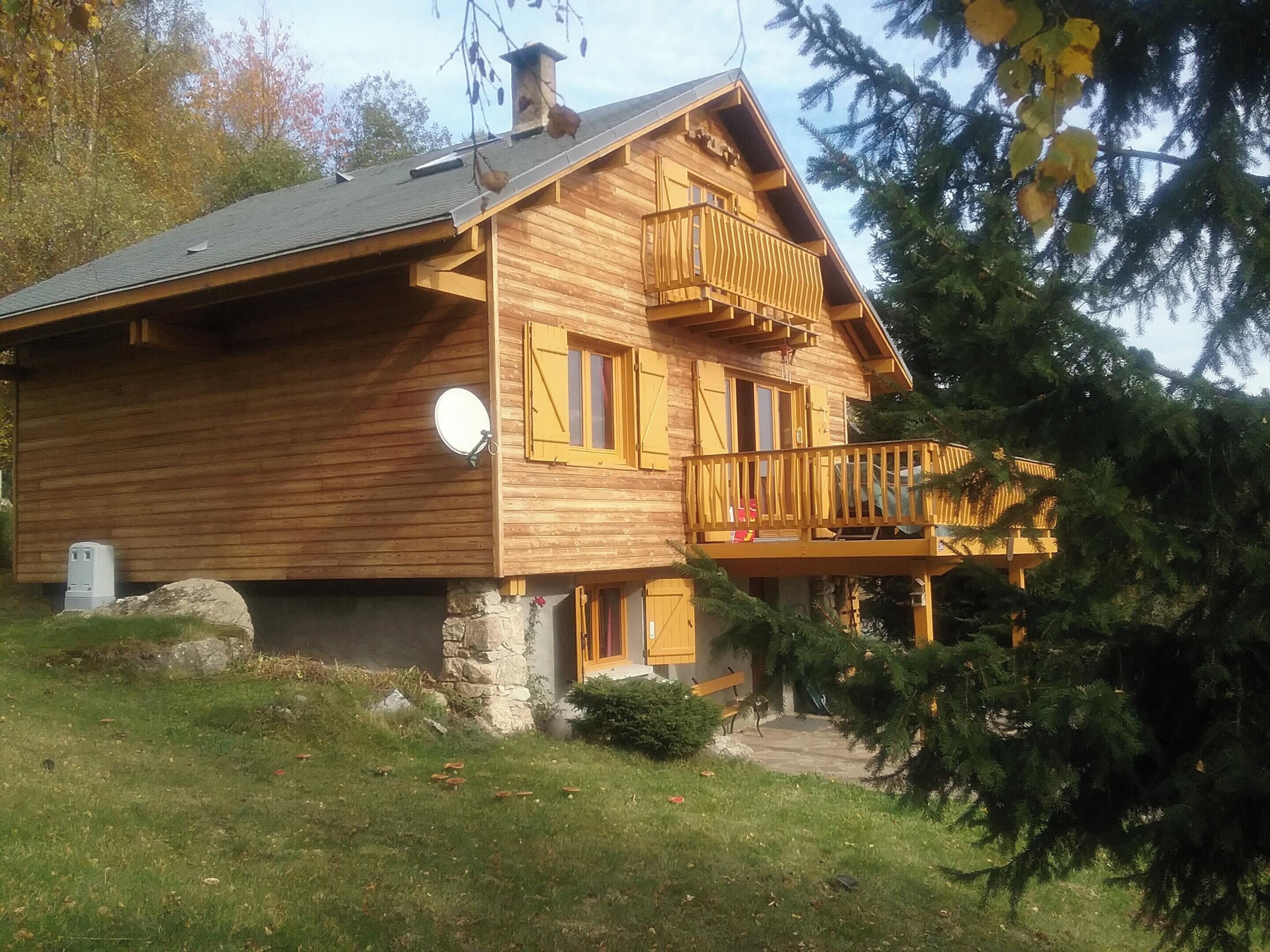 Una cabana de fusta amb un balcó, fonaments de pedra i una petita zona de porxo.