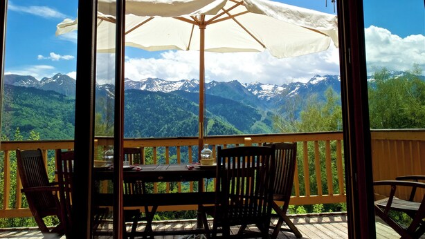 Un balcon avec une table et des chaises, donnant sur un paysage montagneux sous un ciel dégagé.