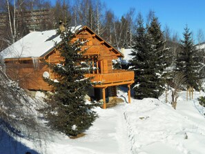 Una cabaña de madera con balcón, rodeada de nieve y árboles.