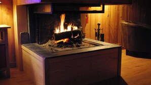 Une cheminée avec des flammes apparentes, un banc en bois à gauche et un mur en bois en arrière-plan.