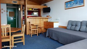 Pieni huone, jossa on pieni keittiönurkkaus, sänky, työpöytä ja televisio.