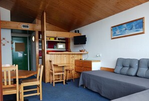Een kleine kamer met een kitchenette, een bed, een bureau en een televisie.