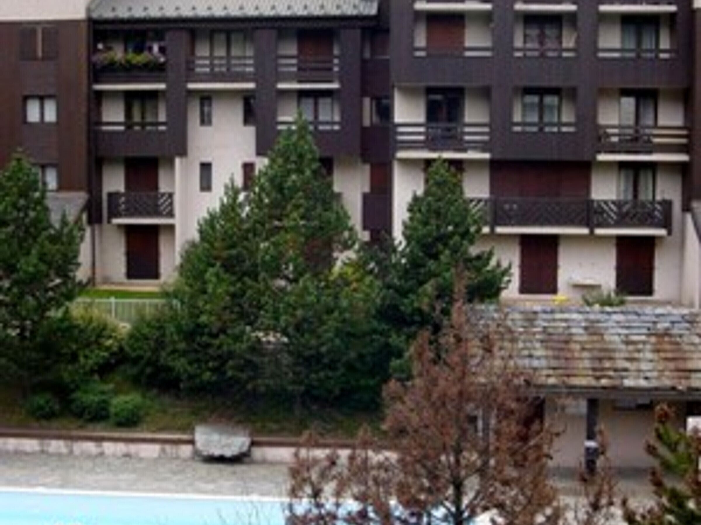 Un immeuble résidentiel à plusieurs étages, doté de balcons, entouré d’arbres et comprenant une piscine.