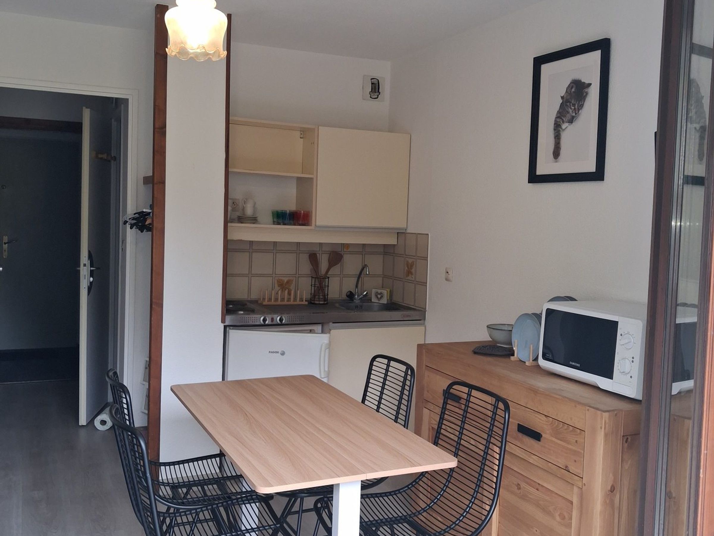 A compact kitchen with a dining table, chairs, a microwave, and a refrigerator.