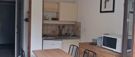 A compact kitchen with a dining table, chairs, a microwave, and a refrigerator.