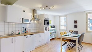 Een moderne keuken met witte kastjes, een magnetron, een oven en een eethoek met een tafel en stoelen.