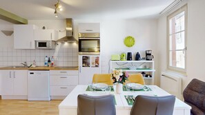 Une cuisine moderne avec des meubles blancs, un four à micro-ondes, un four traditionnel et un coin repas avec une table mise pour deux personnes.
