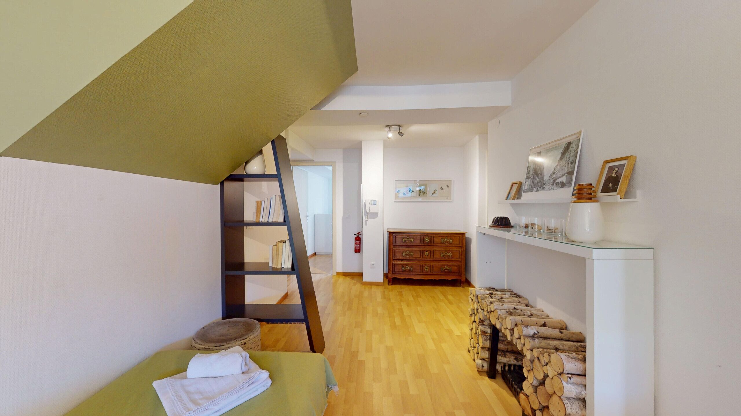 A room with a wooden floor, a green sofa, a wooden ladder, a dresser, and a wall with framed pictures.