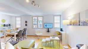 A modern living room with a dining area, a TV mounted on the wall, and a cityscape artwork.