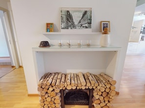 Une pièce comprenant une table à plateau de verre sur laquelle sont exposés une photographie ancienne, une petite sculpture et trois récipients en verre. Sous la table, on trouve un banc sur lequel est rangé du bois de chauffage.