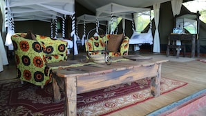 A tented accommodation with a wooden table, patterned sofas, and a woven basket. - Ngorongoro Wild Camps (Ngorongoro)