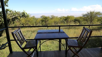 A wooden deck with a table and two chairs, overlooking a grassy landscape with trees and a distant view.