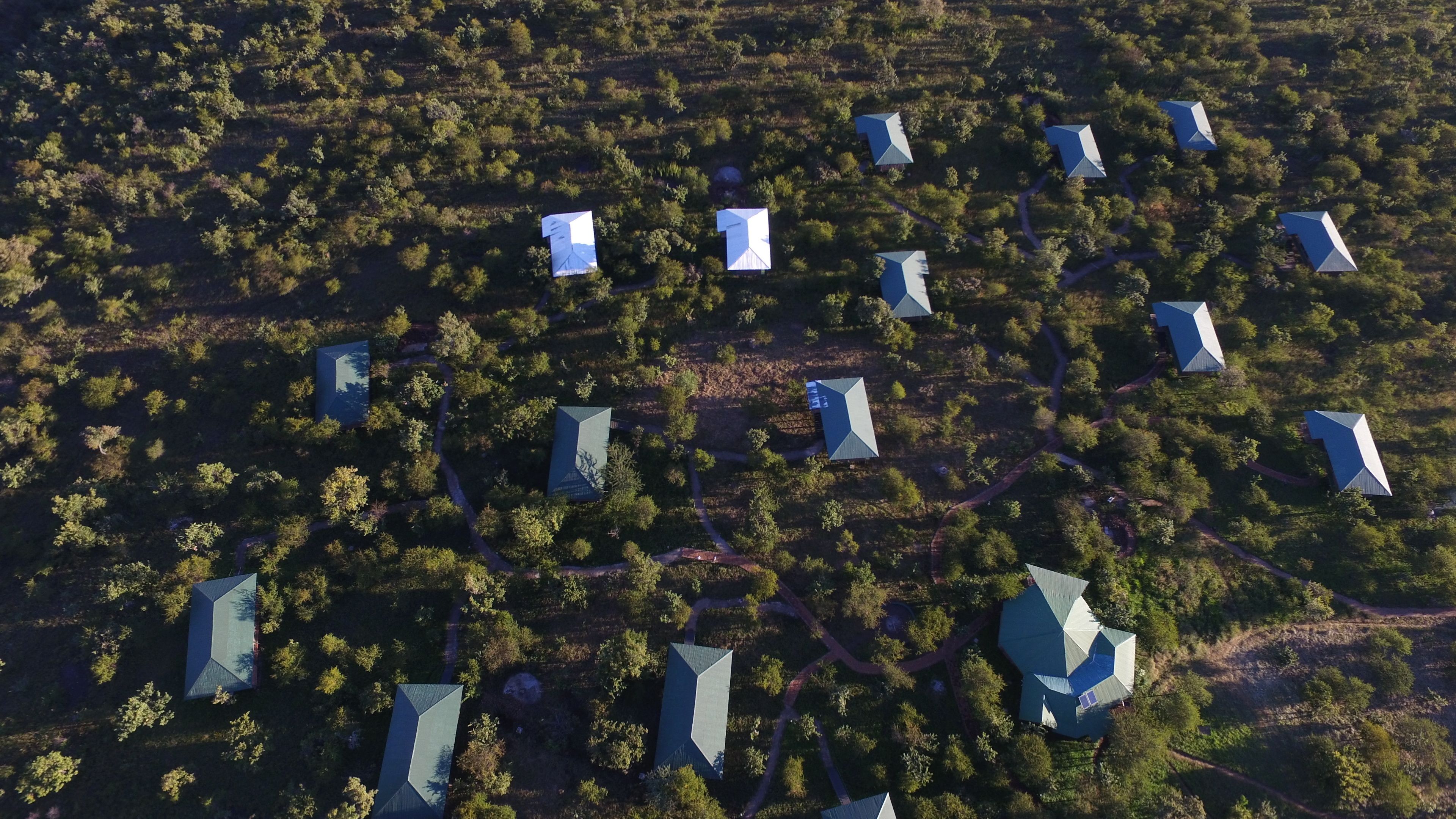 Vue aérienne d’un quartier résidentiel composé de nombreuses maisons aux toits aux formes géométriques, le tout entouré d’une végétation luxuriante.