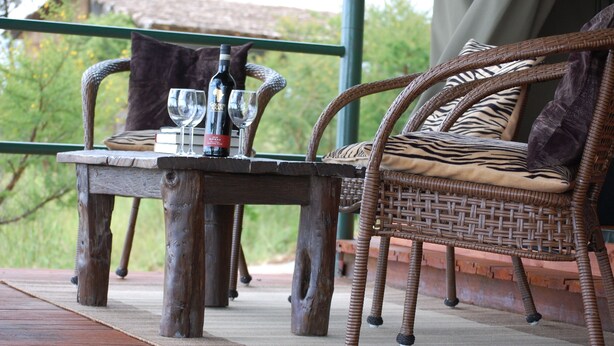 A wicker chair with a zebra-patterned cushion and a table with wine glasses and bottles. - Ngorongoro Wild Camps (Ngorongoro)
