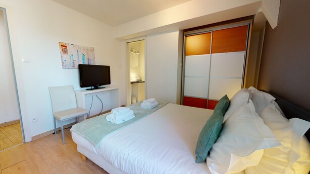 Ein Hotelzimmer mit Bett, Fernseher auf einem Schrank, Stuhl und einem durch eine offene Tür einsehbaren Badezimmer.