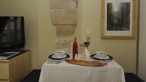 A dining table with a white tablecloth, two white bowls with black designs, a bottle of red wine, a glass of water, a vase with a yellow flower, and a long bread roll. A framed black and white photo hangs on the wall above the table. - A1DG Home Sweet home (París)