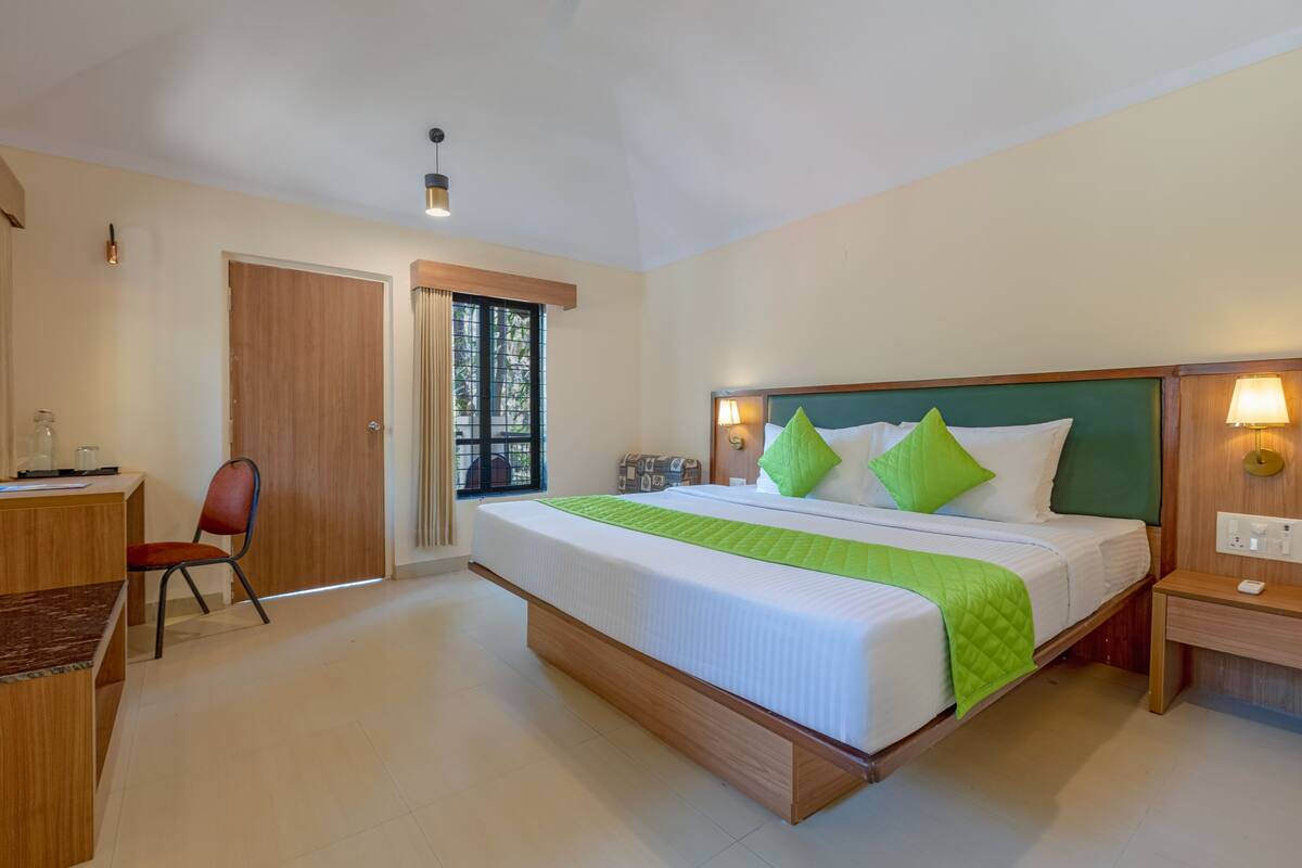 Um quarto com cama, mesa de cabeceira, cadeira, escrivaninha e porta que dá para uma varanda.