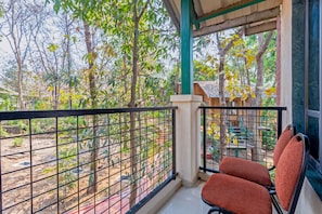 A balcony with a metal railing, a pair of red cushioned chairs, and a view of trees and a building in the background. - Nature Trails Sajan, Vikramgad (Vikramgadh)
