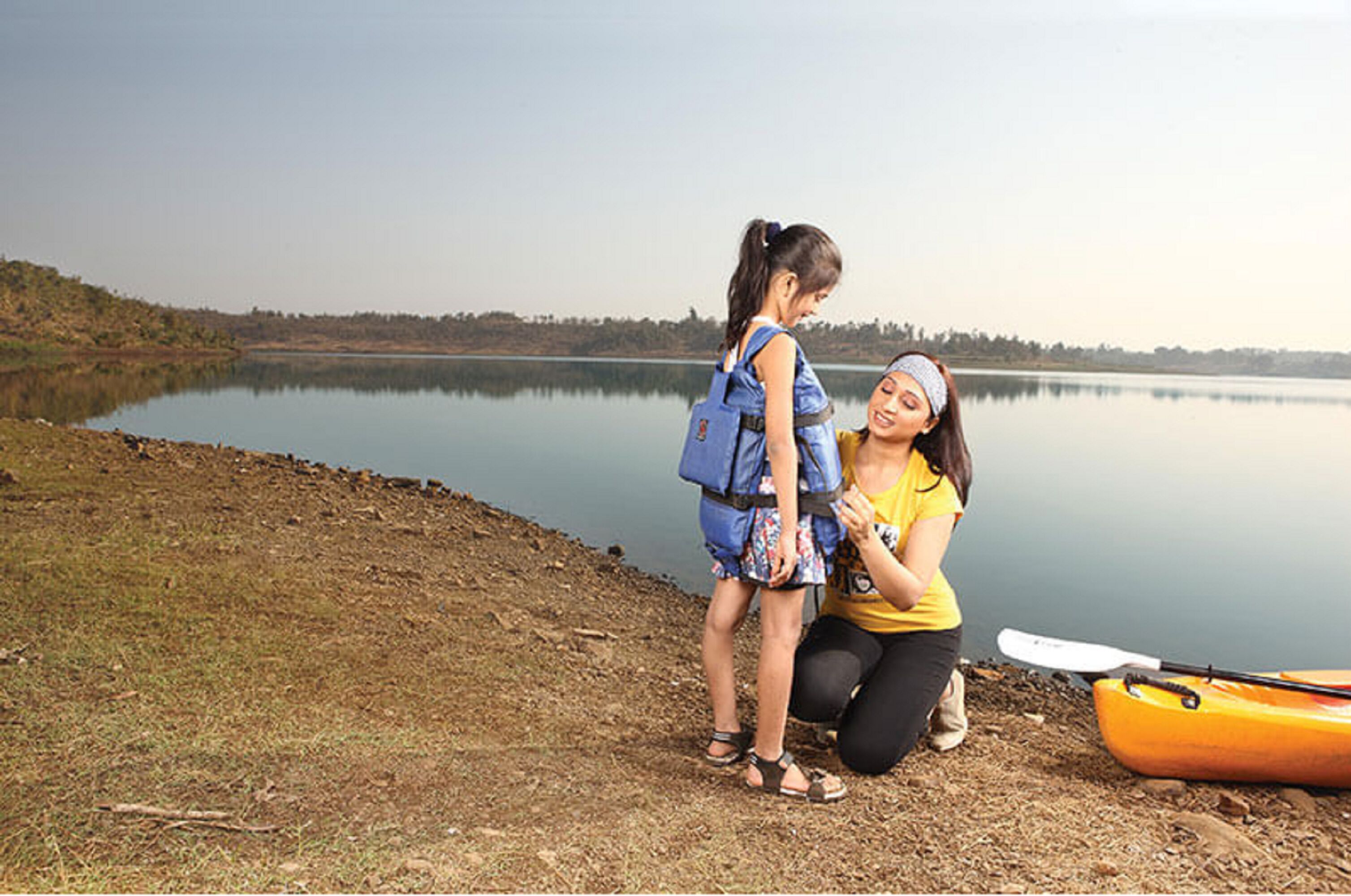 Dos personas junto a un lago tranquilo, con un kayak y una mochila azul.
