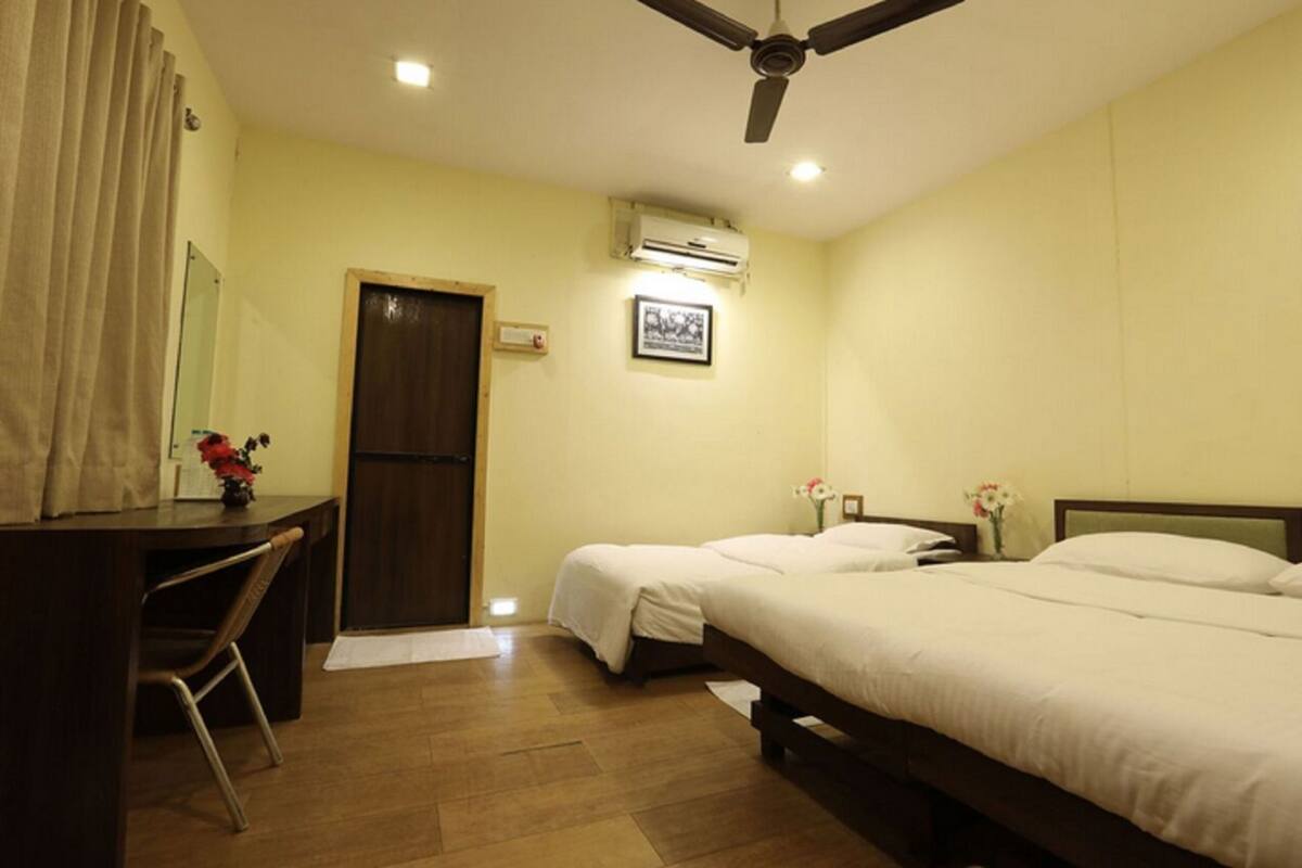 Quarto de hotel com duas camas, uma escrivaninha, uma cadeira, um ventilador de teto e um aparelho de ar condicionado.