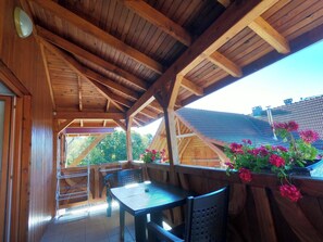 A wooden deck with a table and chairs, a railing, and a view of a house with a sloped roof. - Homerez - Apt. Soultzeren, mountain view (Soultzeren)