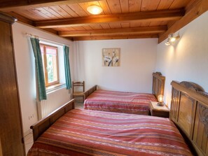 A room with two wooden beds, a window with curtains, a wall-mounted light, and a painting.