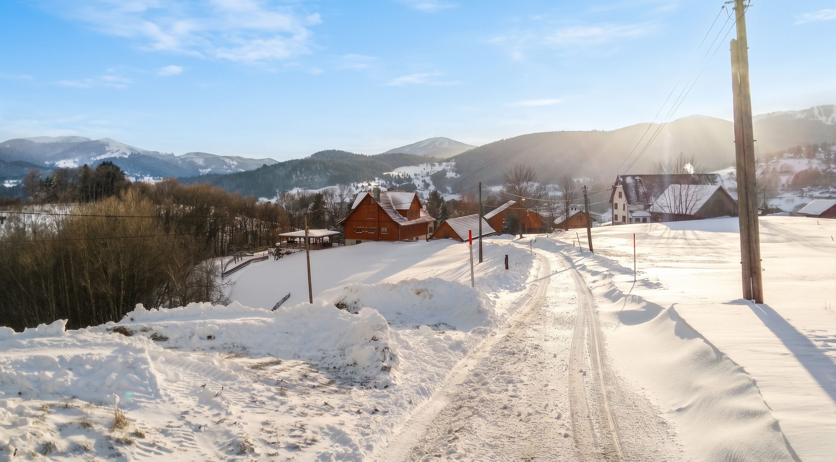 A snow-covered rural landscape with houses, a clear sky, and mountains in the background.