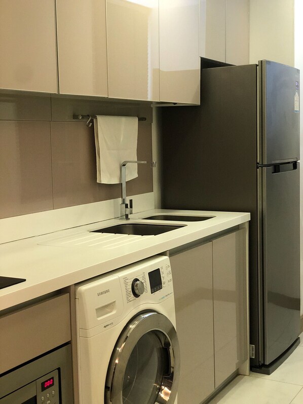 A compact kitchen with a built-in washer, a stainless steel refrigerator, and a sink with a towel hanging on the wall.