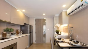 A modern kitchen with built-in appliances, a dining area with a table set for two, and a hallway leading to another room. - Dazzle Residence (Bangkok)