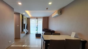 A modern living room with a dining area, a flat-screen TV, and a large window with curtains. - Dazzle Residence (Bangkok)