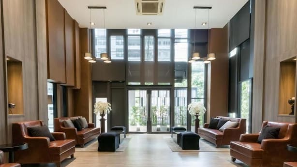 A spacious lobby with leather sofas arranged in a U-shape, large windows, and pendant lighting. - Dazzle Residence (Bangkok)